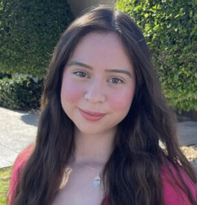 Young woman smiling outdoors in sunlight.